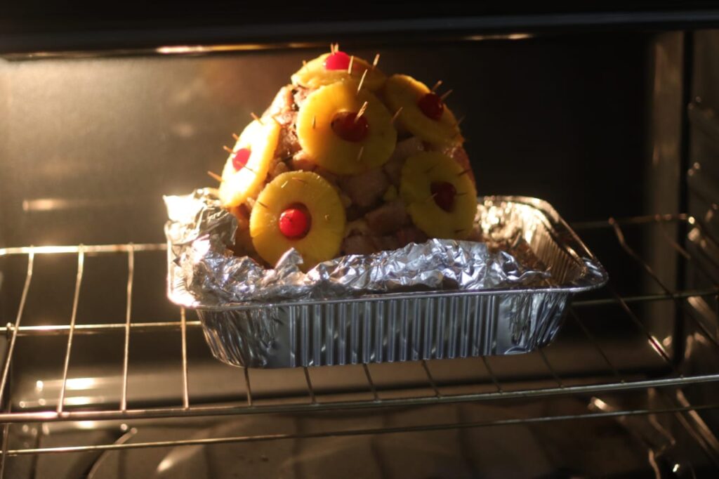 Jamaican Christmas ham baking in the oven with pineapple rings and cherries