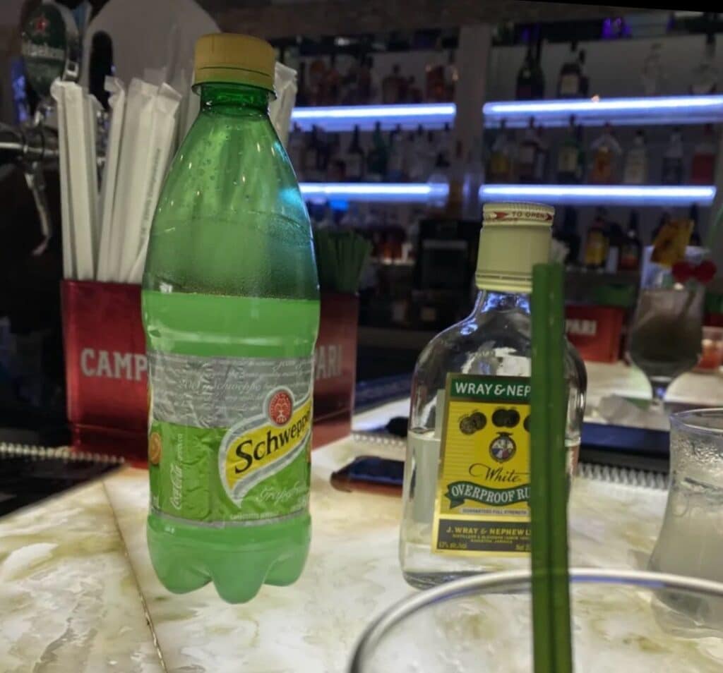 Wray and Nephew White Overproof Rum bottle next to Schweppes grapefruit soda on a bar counter — classic Jamaican rum serve