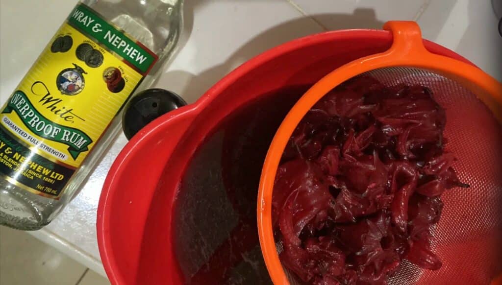 Wray and Nephew White Overproof Rum bottle next to a strainer of freshly pressed sorrel — Jamaican rum in the kitchen