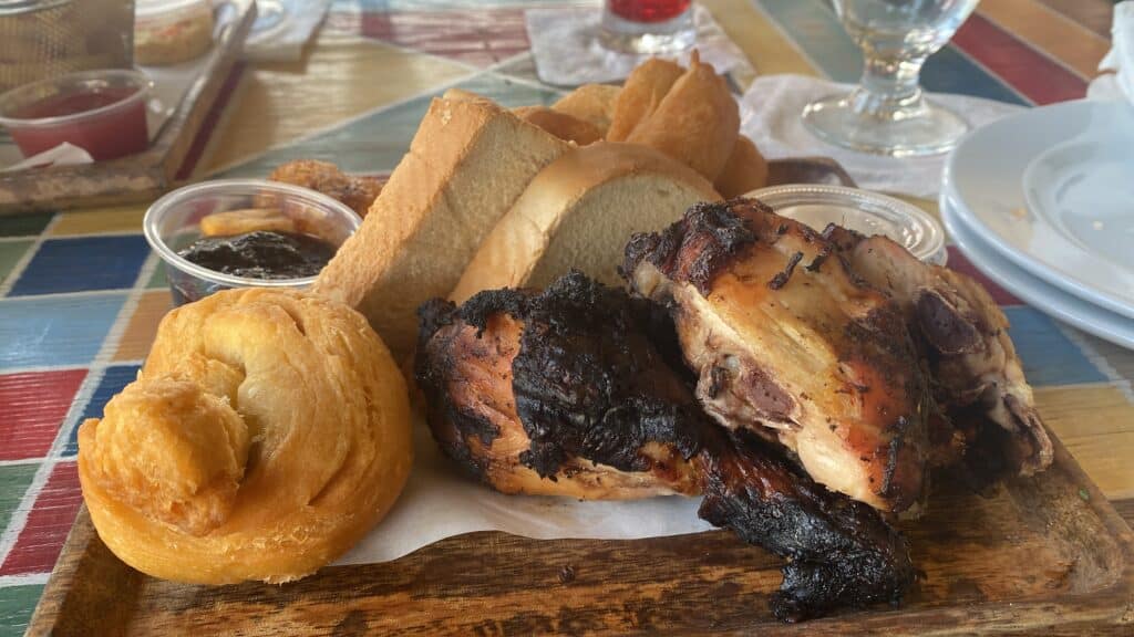 Jamaican jerk chicken served with festival and bread on a wooden board