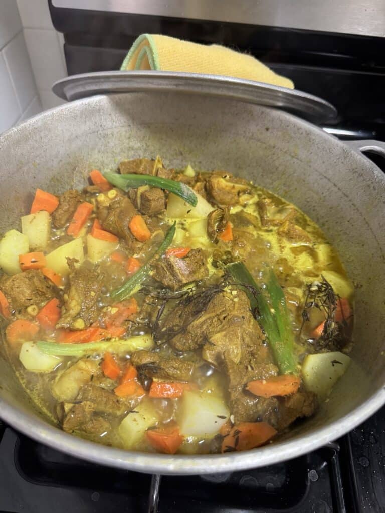 Jamaican curry goat cooking in a Dutch pot with potatoes and carrots
