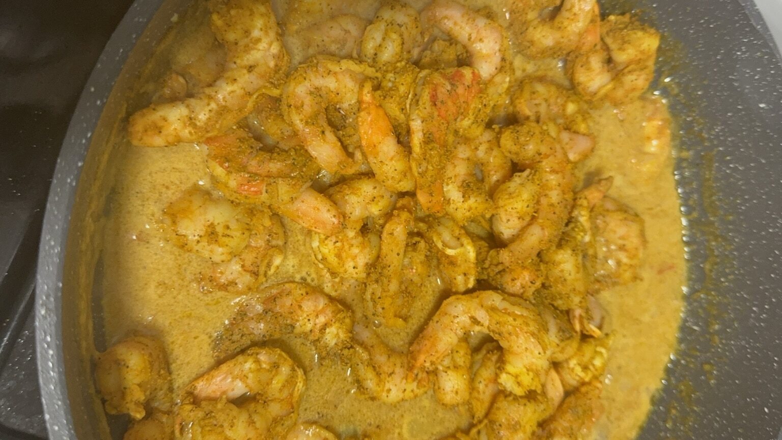Jamaican curry shrimp cooking in a pan with golden curry gravy