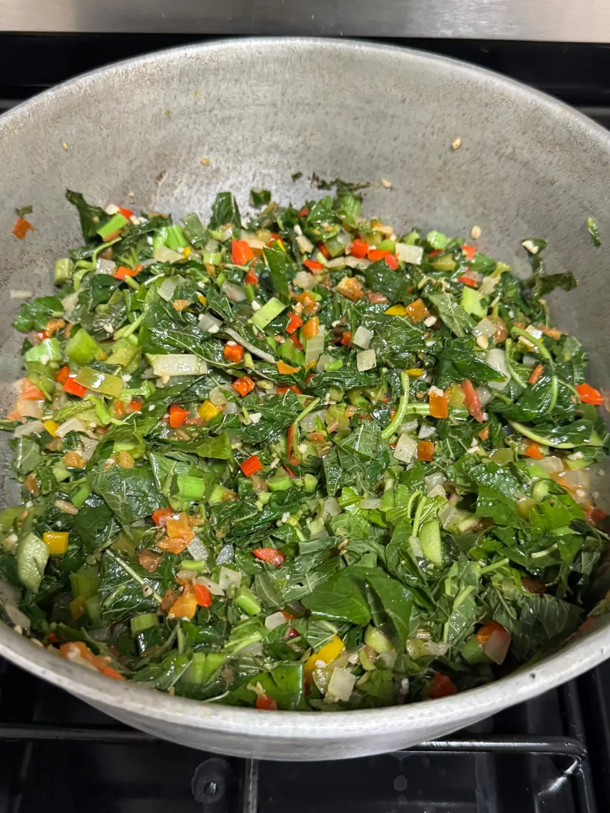 Fresh callaloo leaves wilting and steaming in a Jamaican dutch pot with onion, tomato and sweet pepper