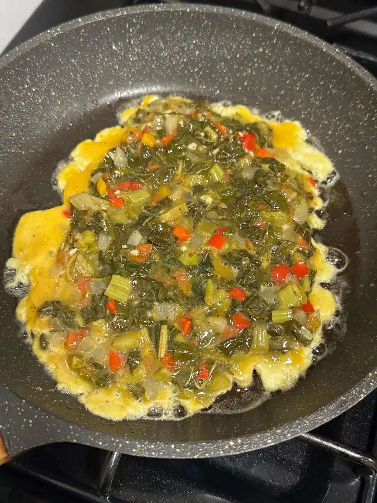Beaten egg mixture with callaloo, tomato, onion and sweet pepper being poured into a pan for a Jamaican callaloo omelette